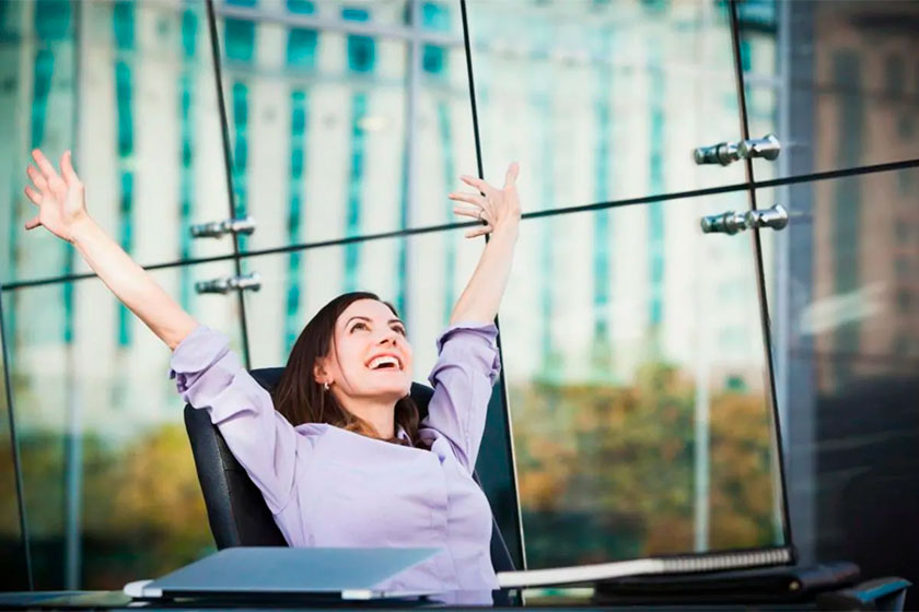 Foto de uma mulher feliz com os braços para cima em seu emprego